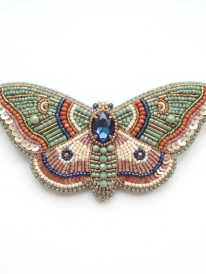 Luna moth hand beaded brooch with sage green, coral, ivory and blue beads, sequins, bugle beads and central blue crystal embellishment.