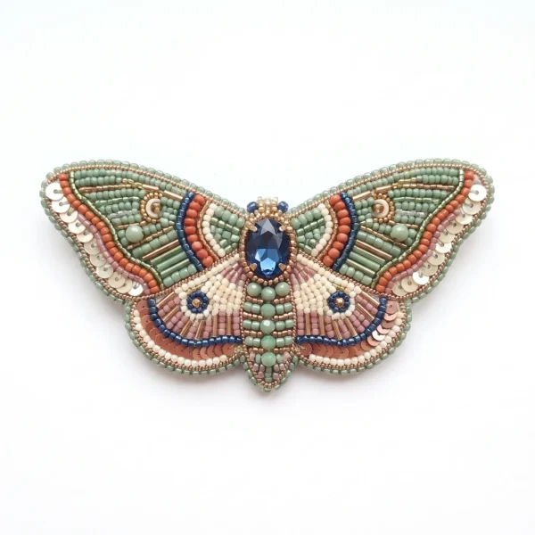 Luna moth hand beaded brooch with sage green, coral, ivory and blue beads, sequins, bugle beads and central blue crystal embellishment.